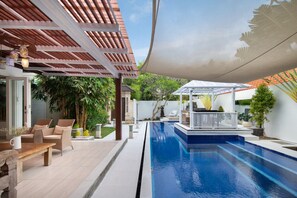 Un área de piscina con una pérgola, mobiliario exterior y un patio cubierto.