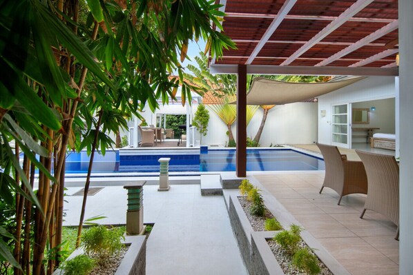 Un área de piscina moderna al aire libre con una pérgola, asientos y vistas a la casa.