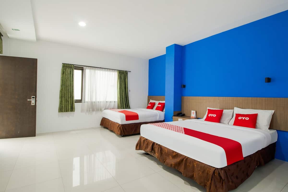A hotel room with two beds, a wooden wardrobe, a window with green curtains, and a blue accent wall.