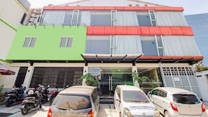 Un edificio de varios pisos con fachada verde y roja, un acceso cubierto y varios coches estacionados.