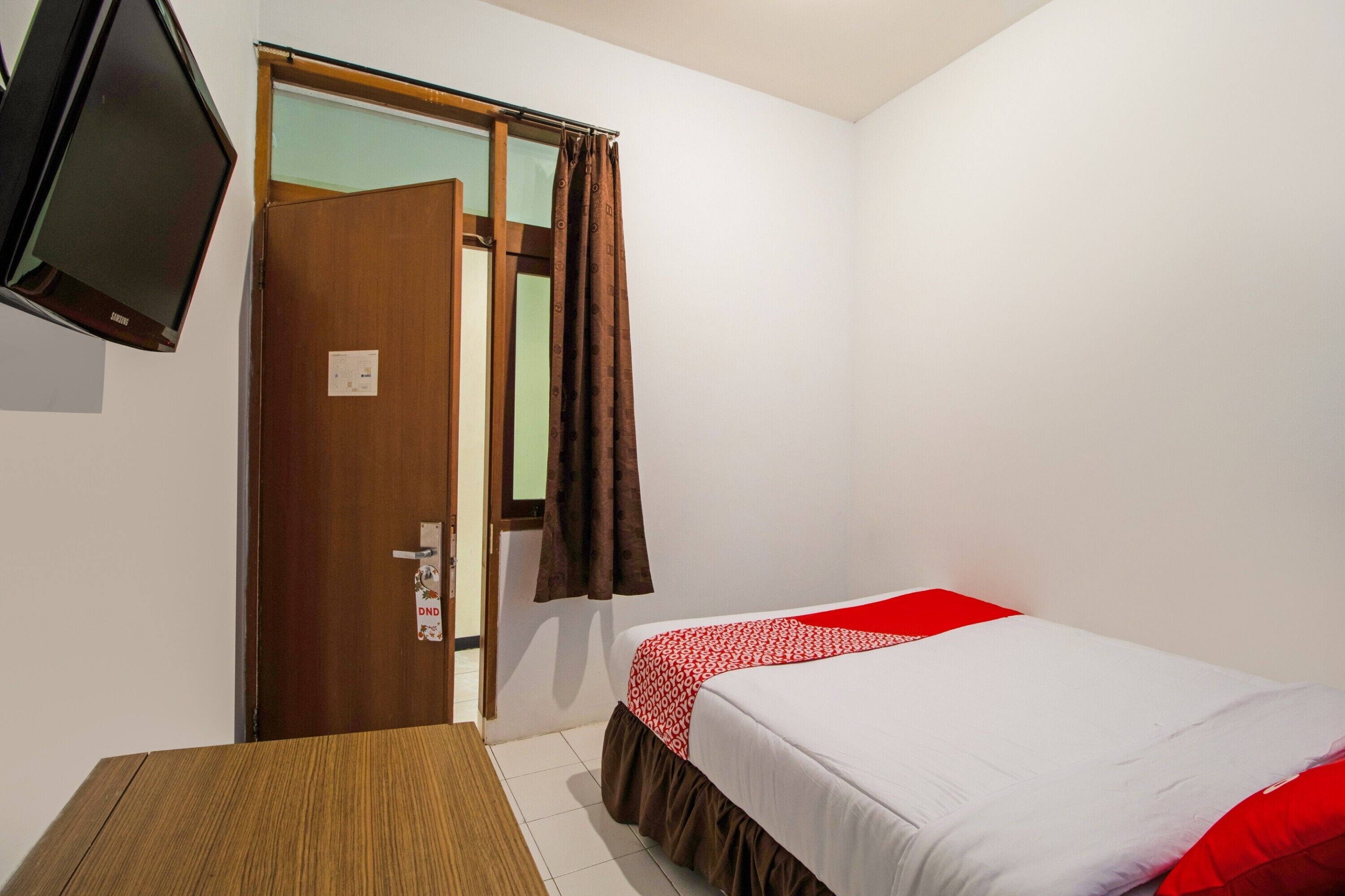 A room with a bed, a wooden table, and a television mounted on the wall.