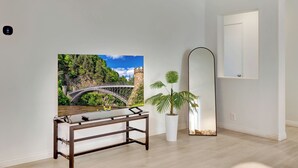 Una habitación moderna con un banco de madera, un cuadro grande de un puente, una planta de palma en maceta y un espejo fijado a la pared.