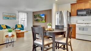 Una cocina moderna con comedor, armarios de madera, electrodomésticos de acero inoxidable y un amplio ventanal con vista a un puente.