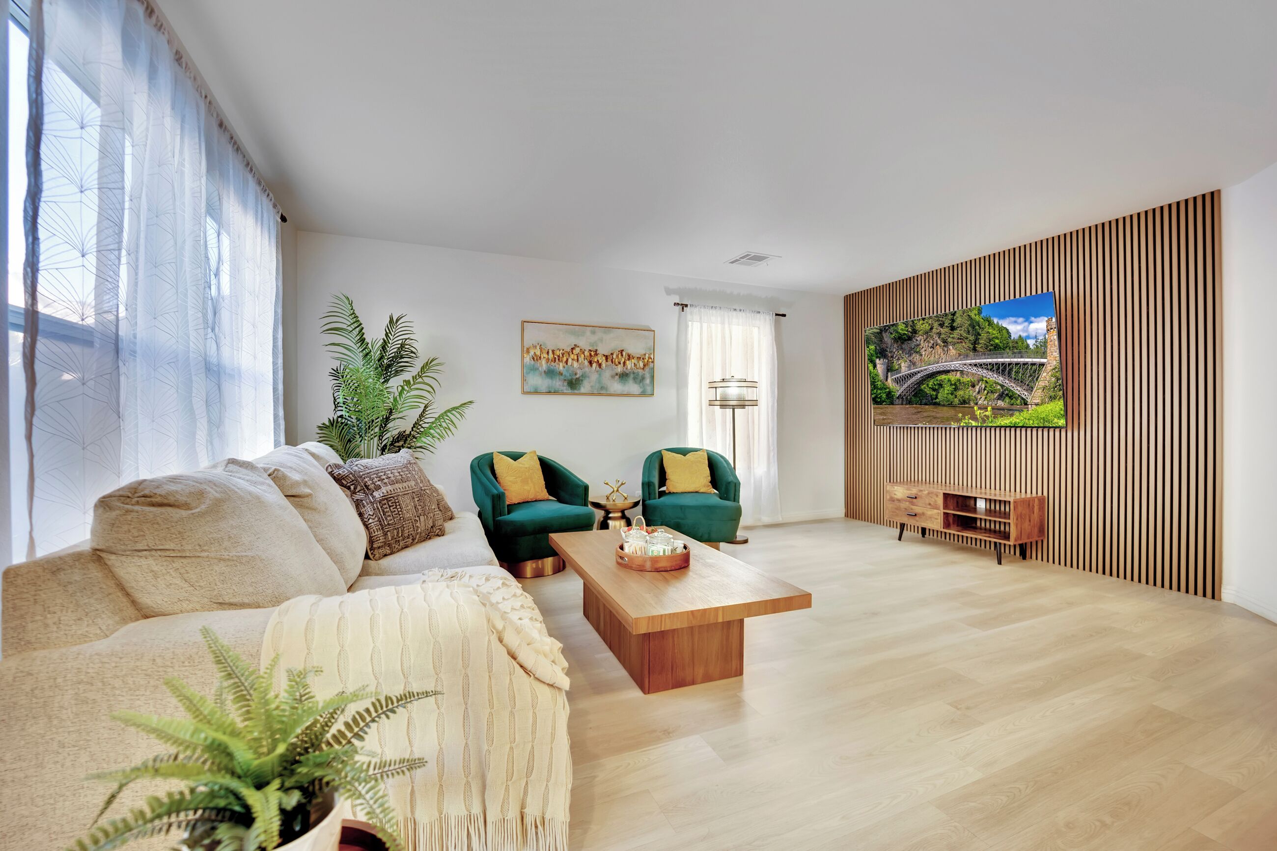 A modern living room with a sofa, two armchairs, a coffee table, and a TV on the wall.