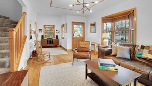 A spacious living room with a staircase, a leather sofa, a wooden coffee table, and a bookshelf.