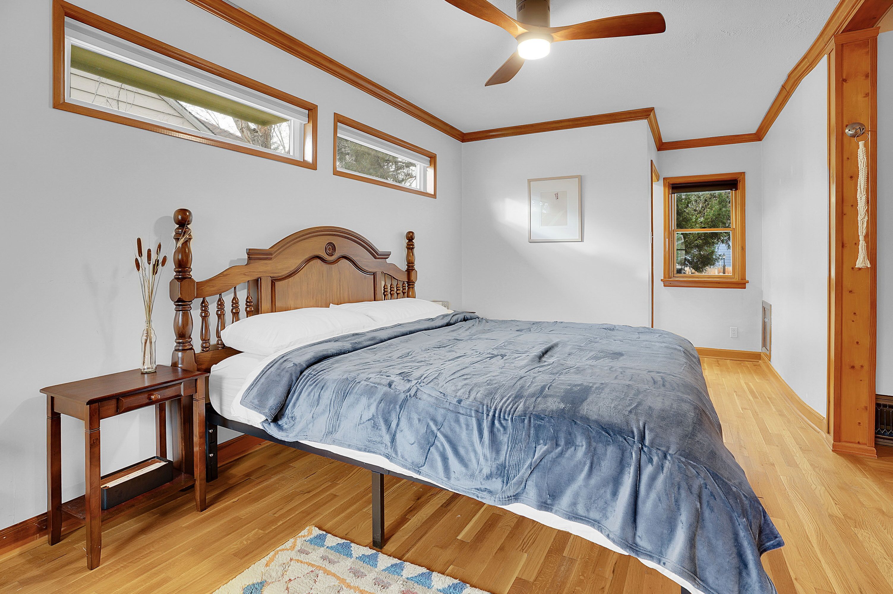 A bedroom with a wooden bed, a nightstand, a ceiling fan, and two windows.