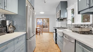 A modern kitchen with stainless steel appliances, a herringbone wood floor, and a view to the outside.