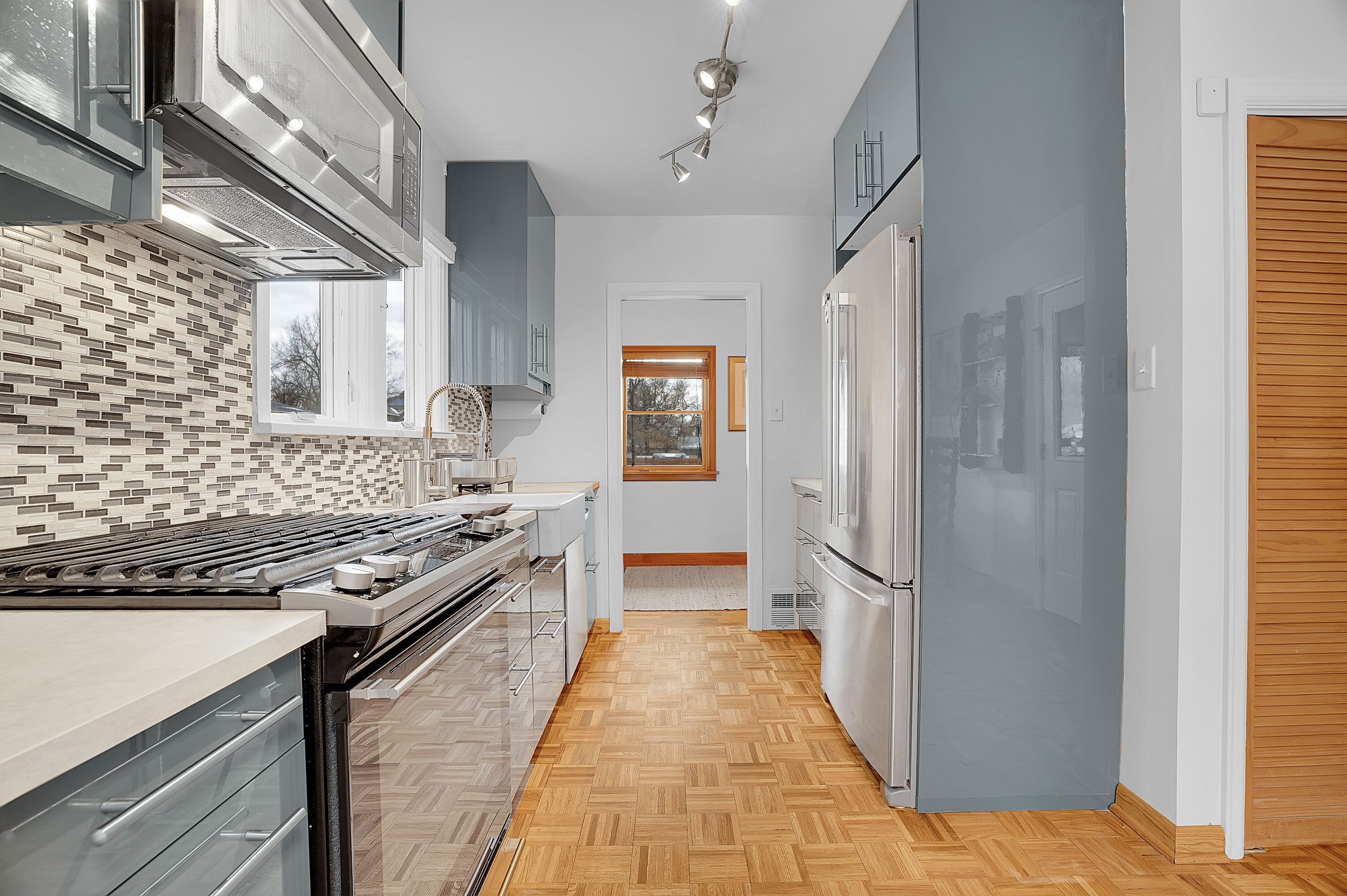 Et moderne køkken med et backsplash i fiskebensmønster, rustfrie stål-apparater og trægulv.