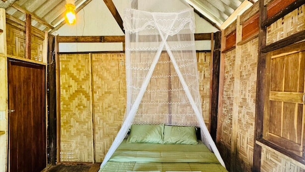 Quarto com uma cama, mosquiteiro e paredes de madeira.