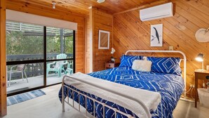 Een slaapkamer in een houten chalet met een bed, een nachtkastje, een lamp en uitzicht op het terras.