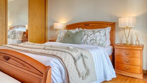 A neatly made bed with a wooden headboard, a bedside table with a lamp, and a nightstand with a lamp. - Funchal Atrium, a Home in Madeira (Funchal)