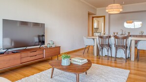 A modern living room with a flat-screen TV, wooden coffee table, and a dining area with a white tablecloth and chairs. - Funchal Atrium, a Home in Madeira (Funchal)