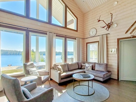 A spacious living room with large windows, a sofa, chairs, and a round coffee table.