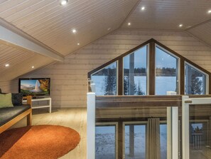 A spacious living area with a high ceiling, a large window overlooking a snowy landscape, a television on a stand, and a cozy orange rug. - Rantatähti by Interhome (Pudasjärvi)