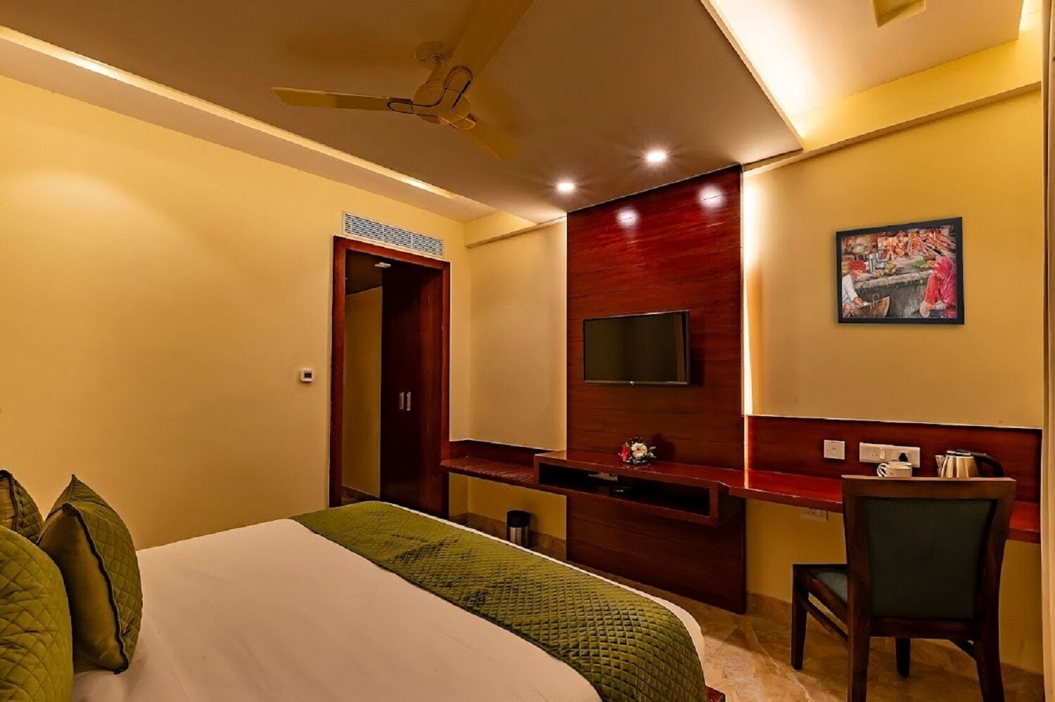 A hotel room with a bed, a desk, a chair, a television, and a painting on the wall.