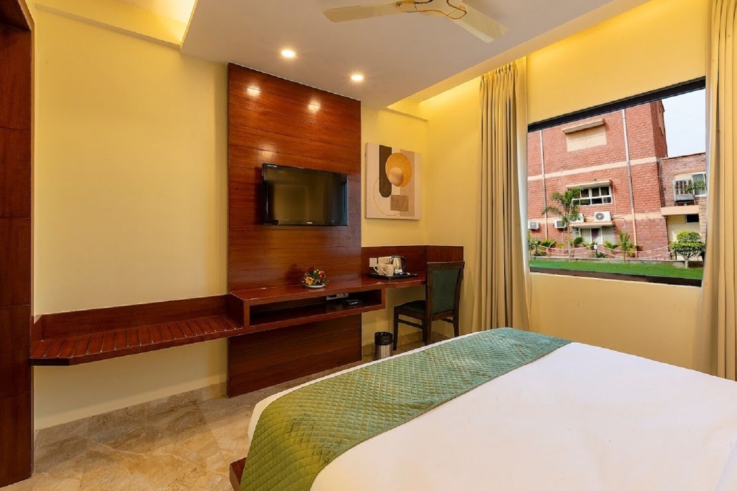 A hotel room with a bed, a desk with a chair, a television, and a window with a view of a building.