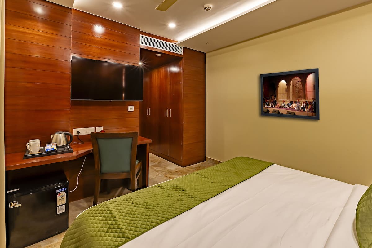 Ein Hotelzimmer mit Bett, Schreibtisch, Sessel, Fernseher und einem Theaterbild.