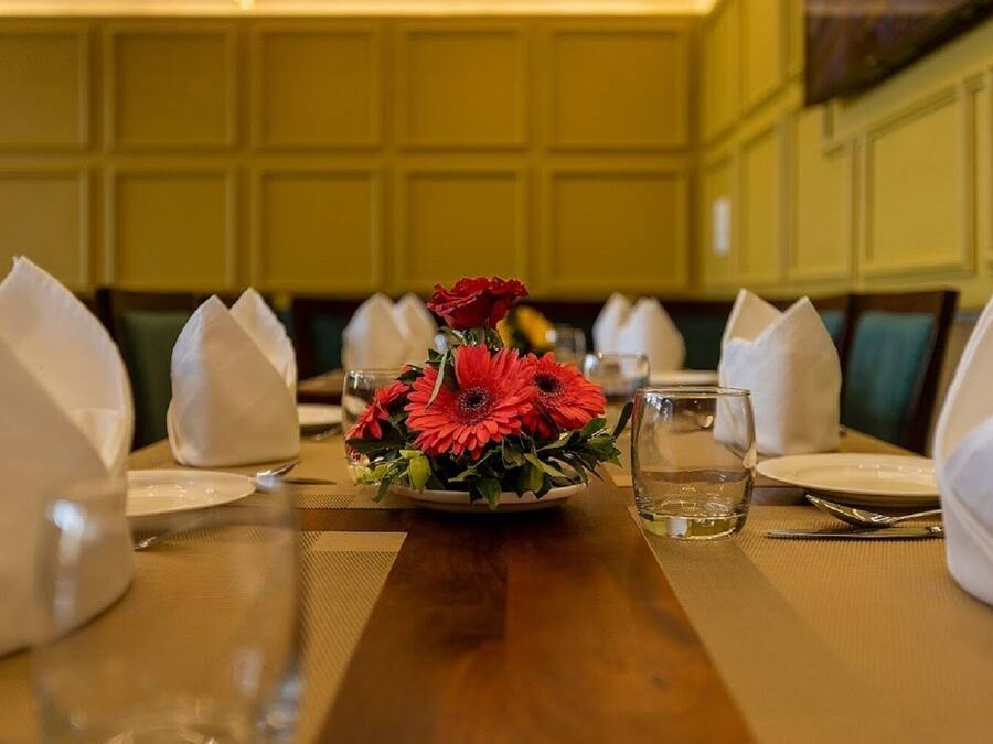 Een eettafel gedekt met witte servetten, een glas water en een bloemstuk met rode bloemen.