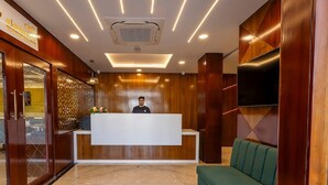 A hotel reception area with a wooden reception desk, a green sofa, and a flat-screen TV mounted on the wall. - Mertiya Residency (Jodhpur)