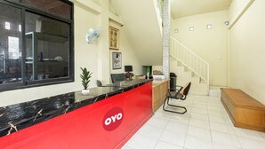 A reception area with a red counter, a staircase, and a wooden bench. - Hotel O Delta Bnb Residence Syariah (Prabumulih)