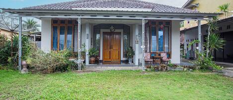 A house with a tiled roof, a wooden front door, and a covered porch with potted plants.