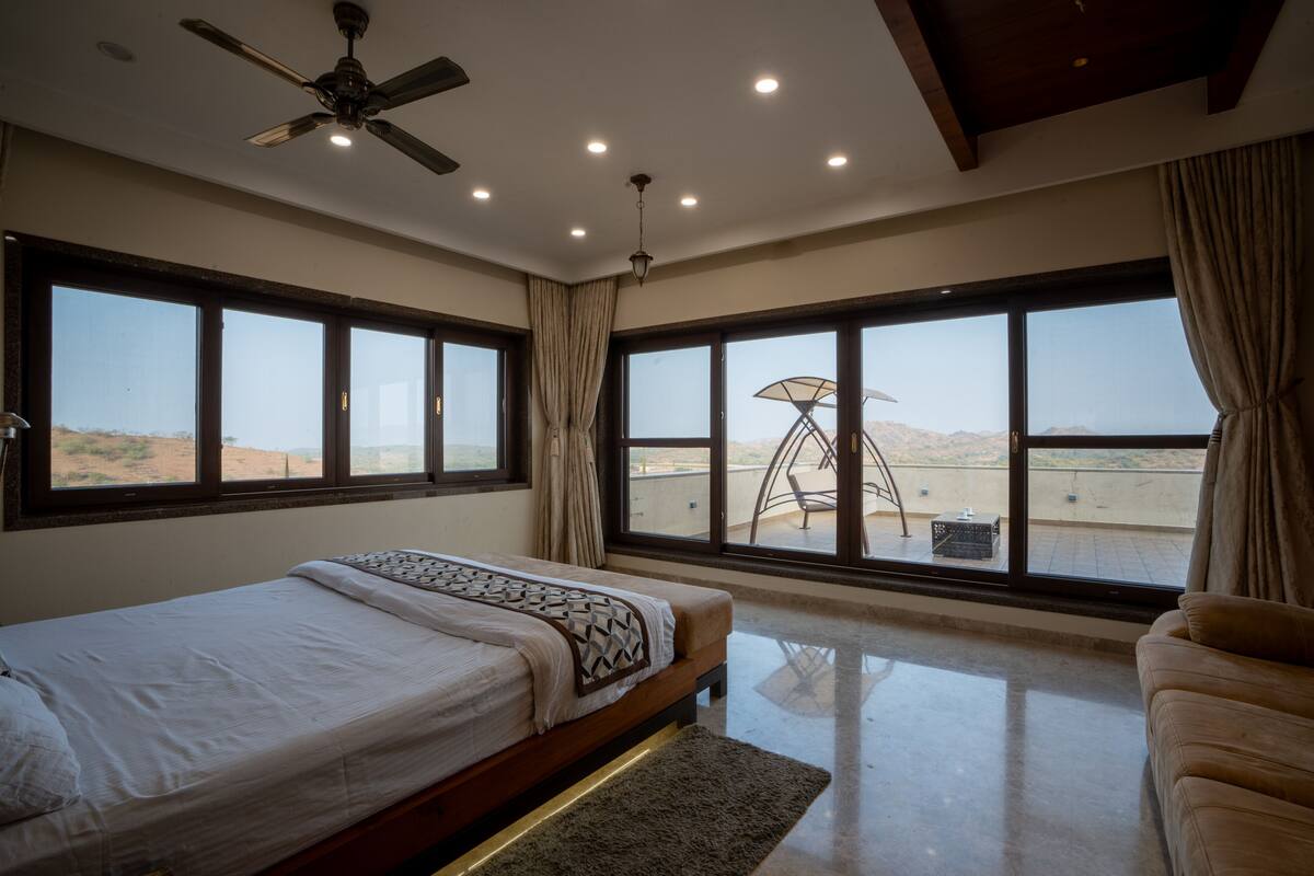 A bedroom with a bed, a ceiling fan, large windows, and a view of the landscape.