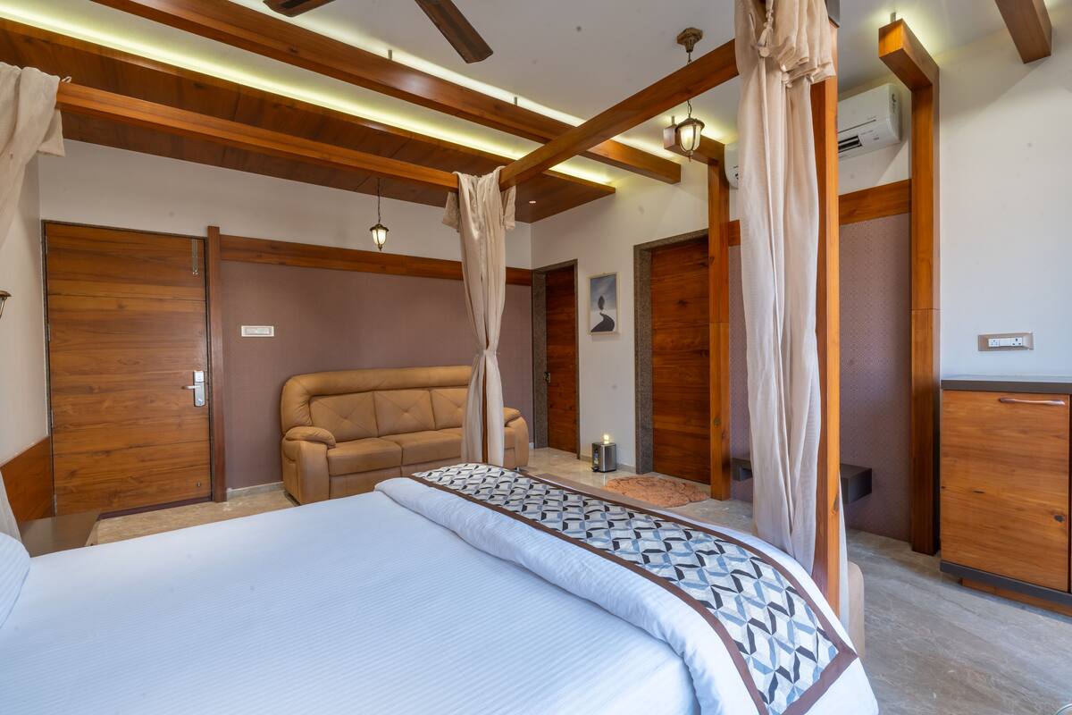 A bedroom with a large bed, a sofa, wooden beams, and a wardrobe.