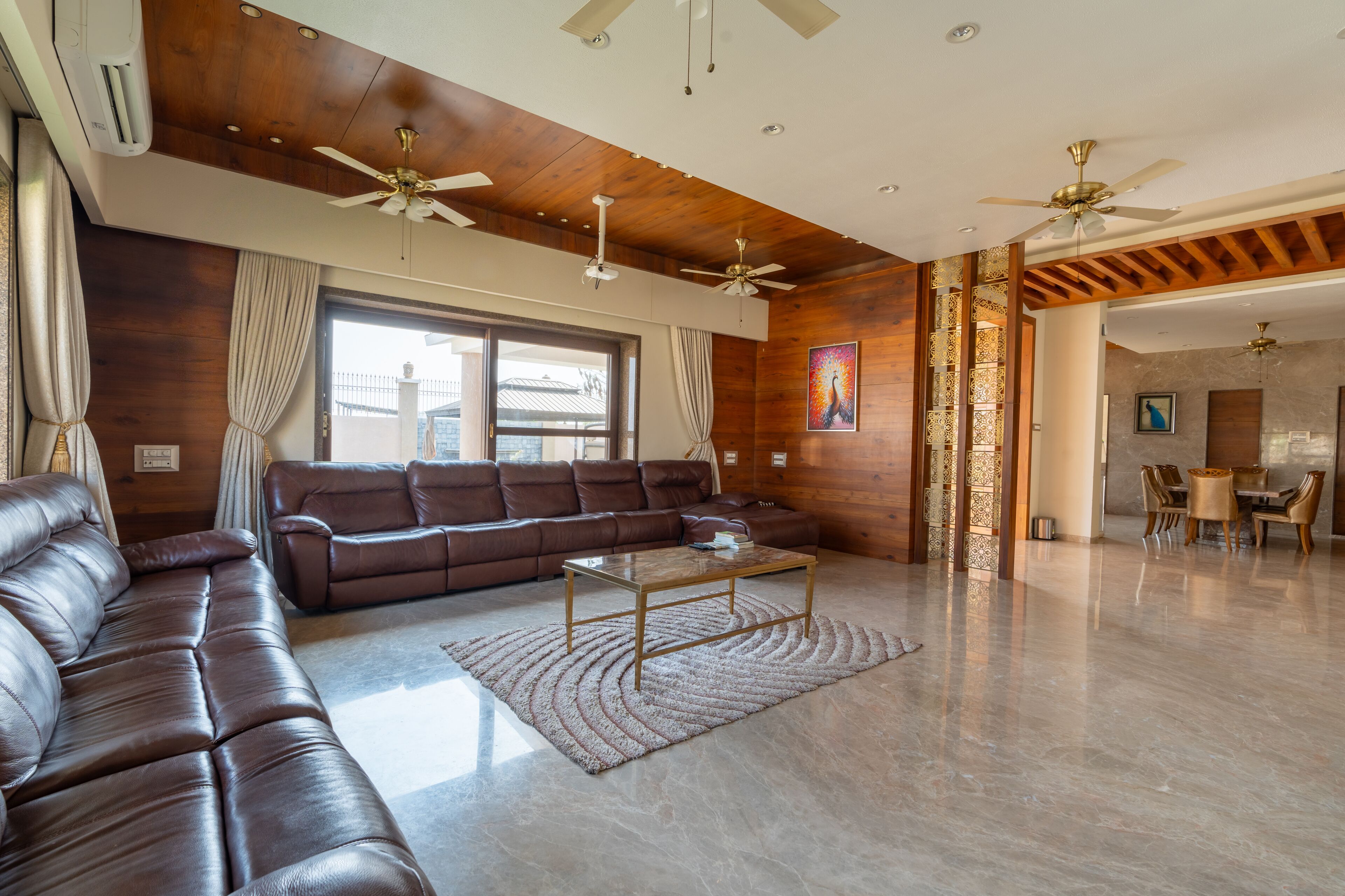 A spacious living room with a brown leather sofa, a glass coffee table, and a ceiling fan.