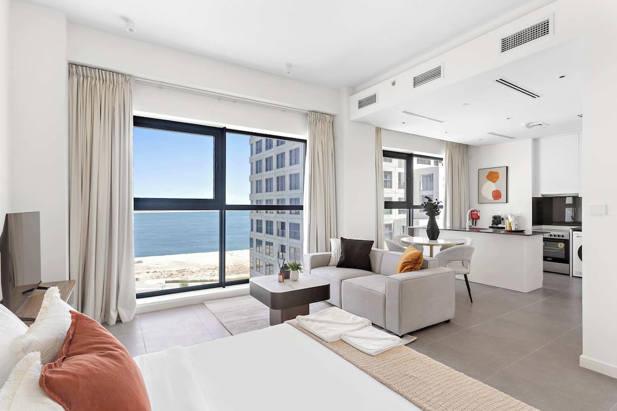 A modern hotel room with a large balcony, a kitchenette, and a view of the sea.