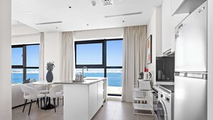 Eine moderne Küche mit einer zentralen Kochinsel, einer integrierten Waschmaschine und großen Fenstern mit Meerblick.