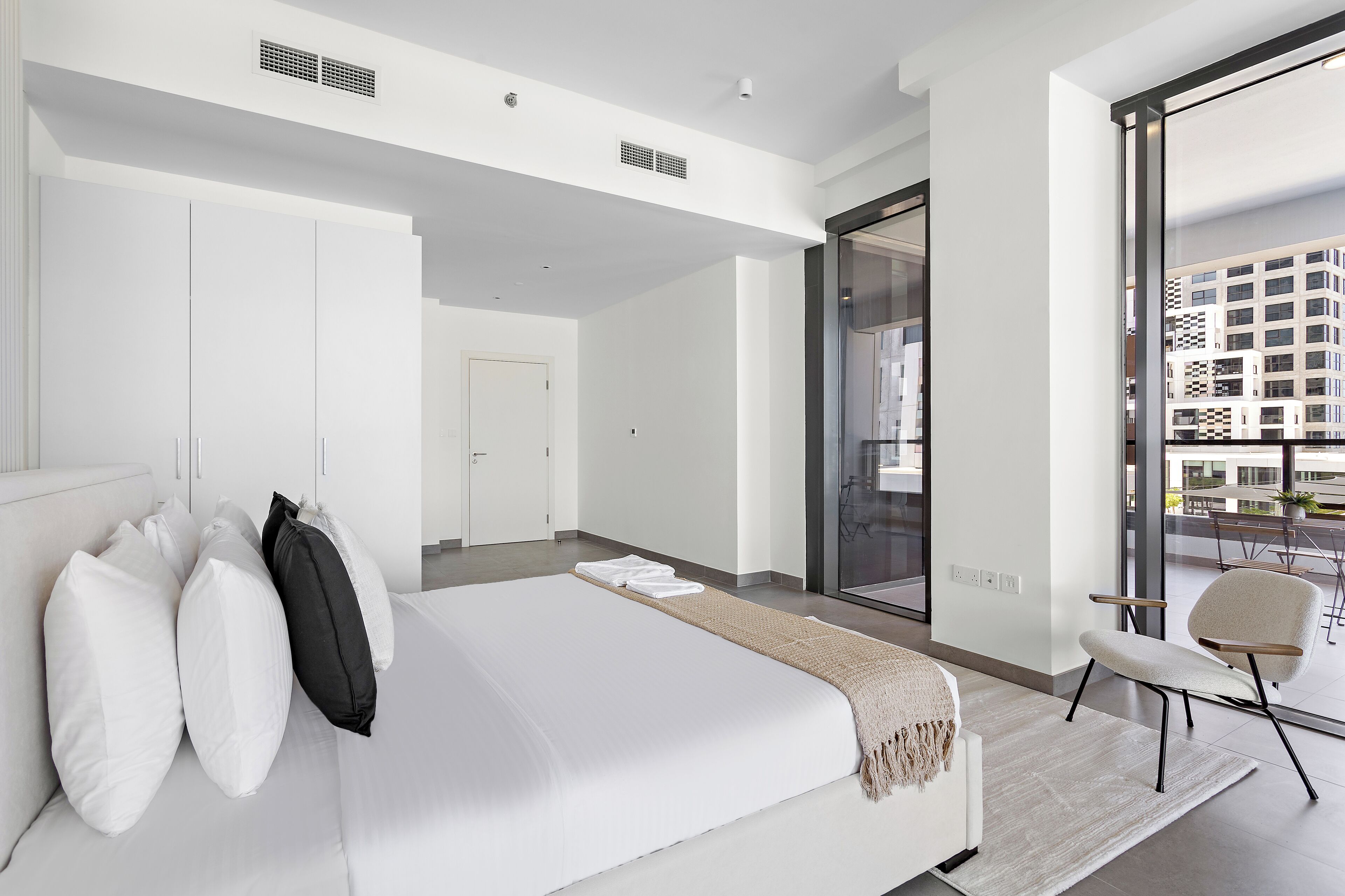 A modern hotel room with a large bed, a seating area, and a view of the city through large windows.