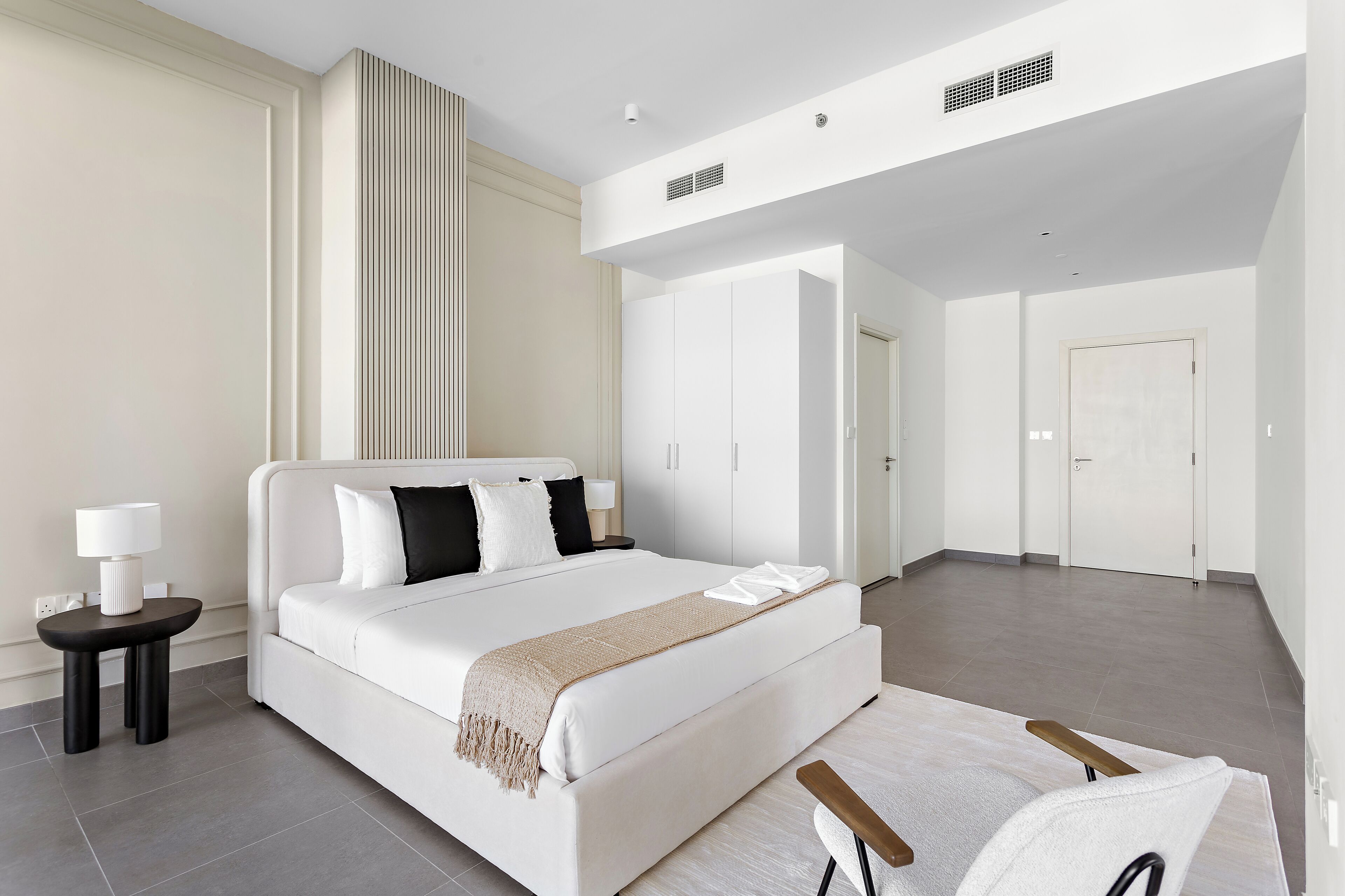A modern hotel room with a large bed, a bedside table with a lamp, and a view of the hallway.