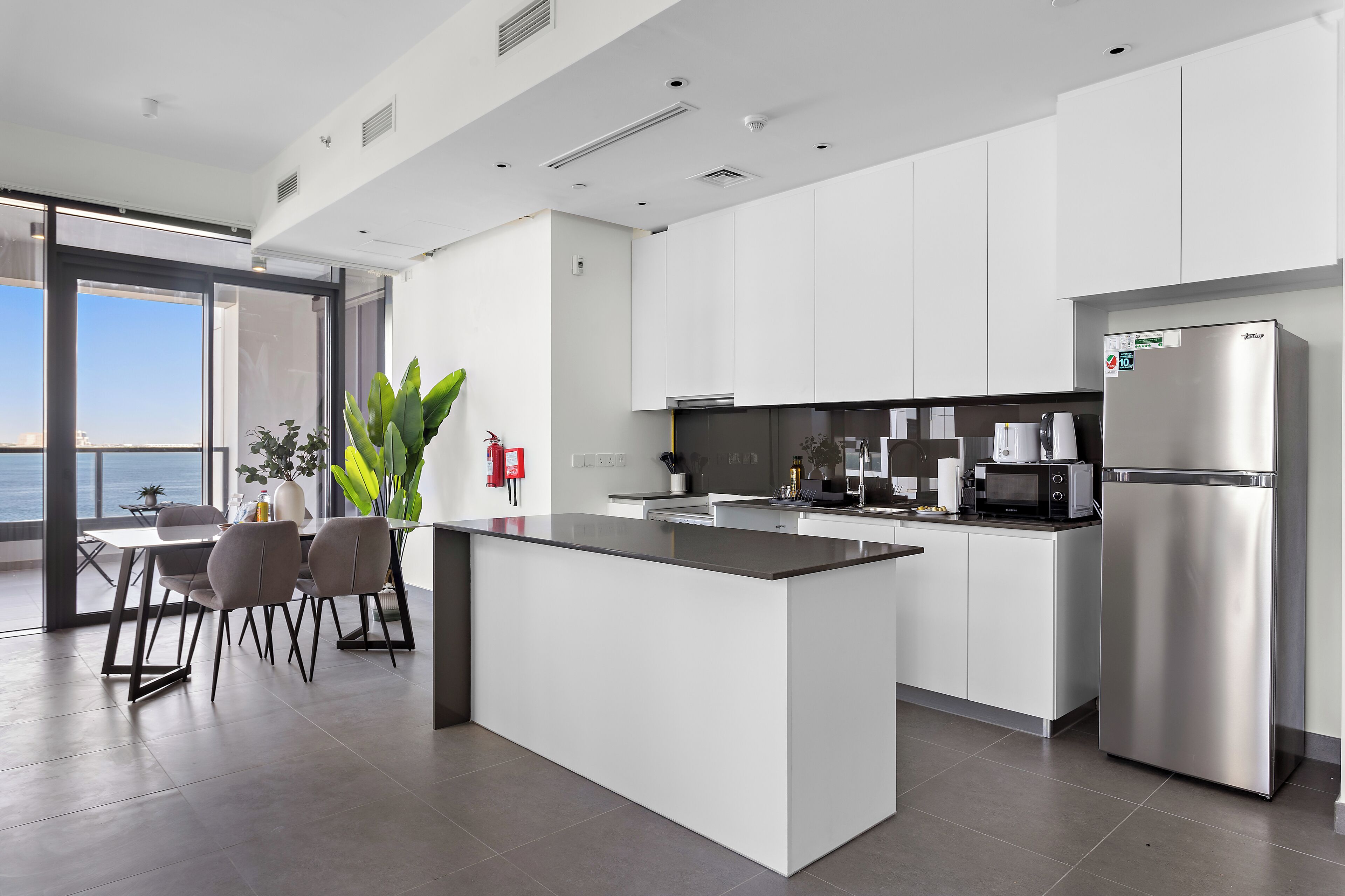 A modern kitchen with a central island, stainless steel appliances, and a view of the sea.