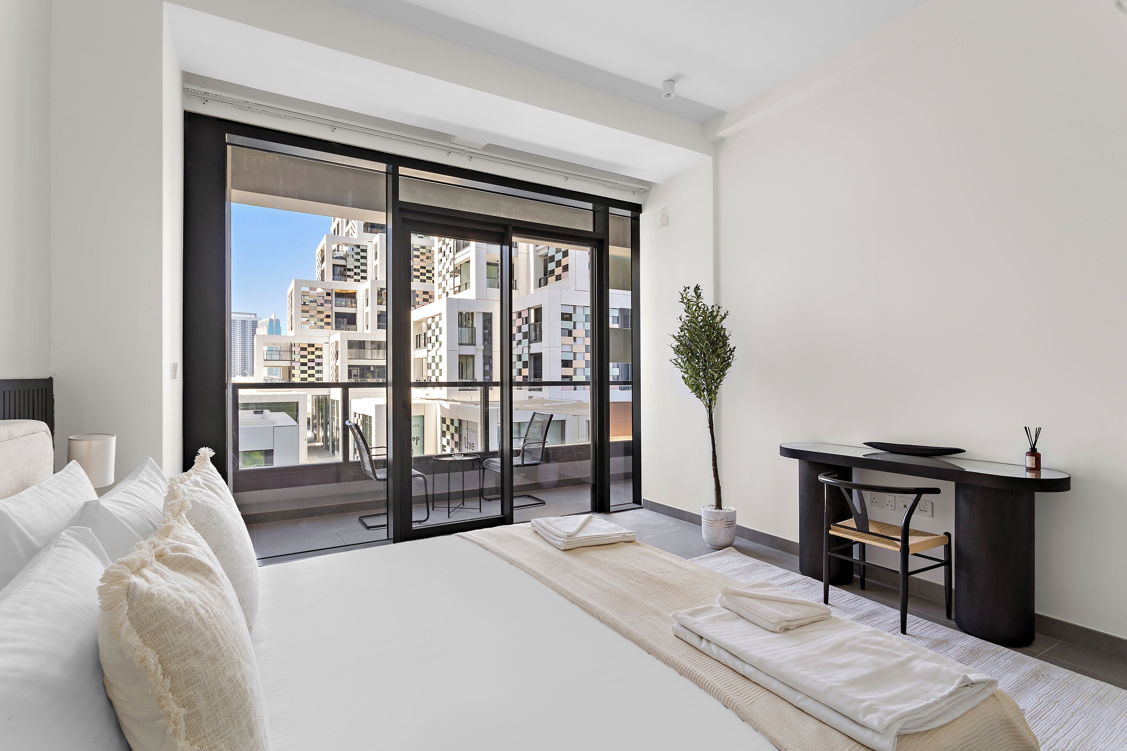 A modern hotel room with a large bed, a desk, and a balcony with a city view.