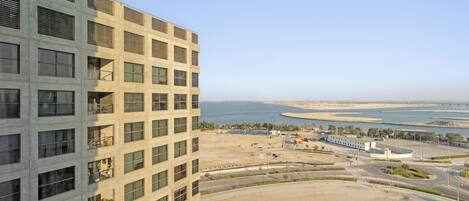 A high-rise building with multiple balconies overlooking a coastal area with a marina and sandy terrain.