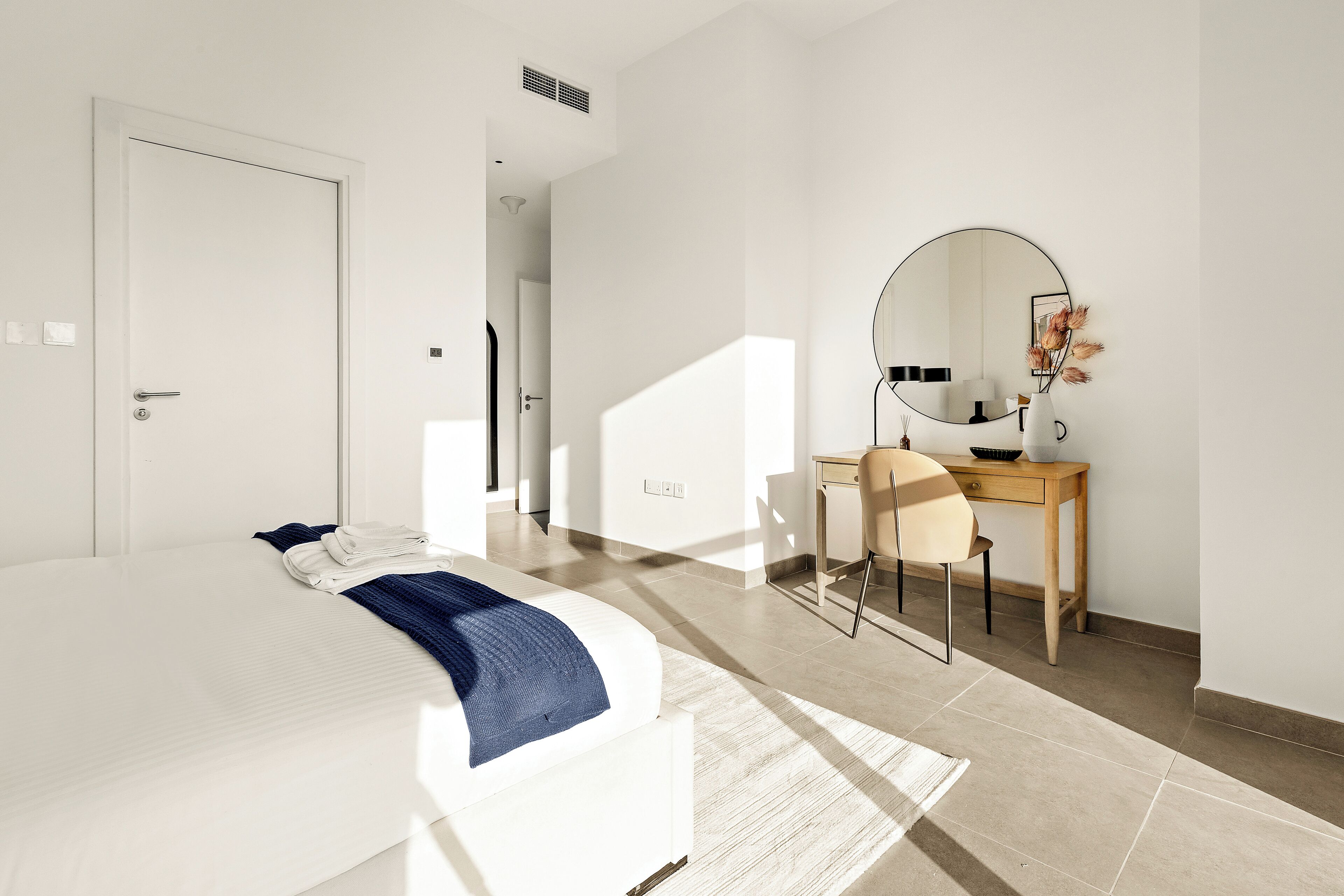 Quarto de hotel moderno com uma cama bem arrumada, uma escrivaninha com cadeira e um espelho grande na parede.