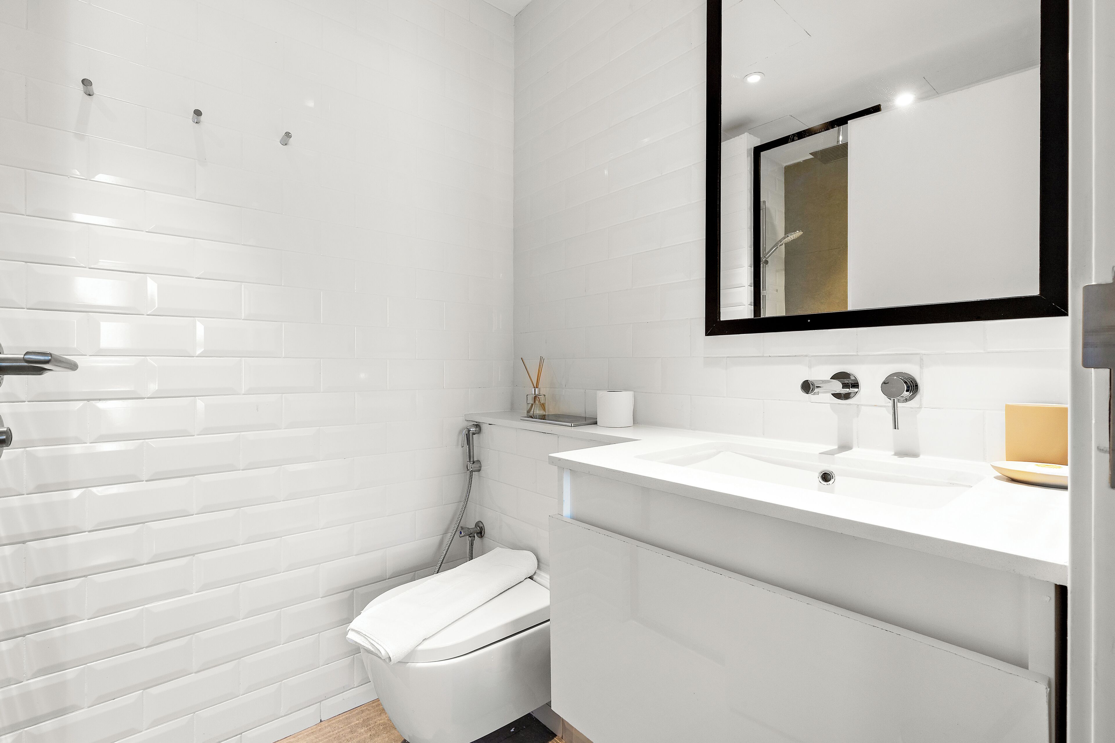 Un bagno moderno con piastrelle bianche tipo metro, un WC bianco, un lavandino con specchio e una zona doccia.