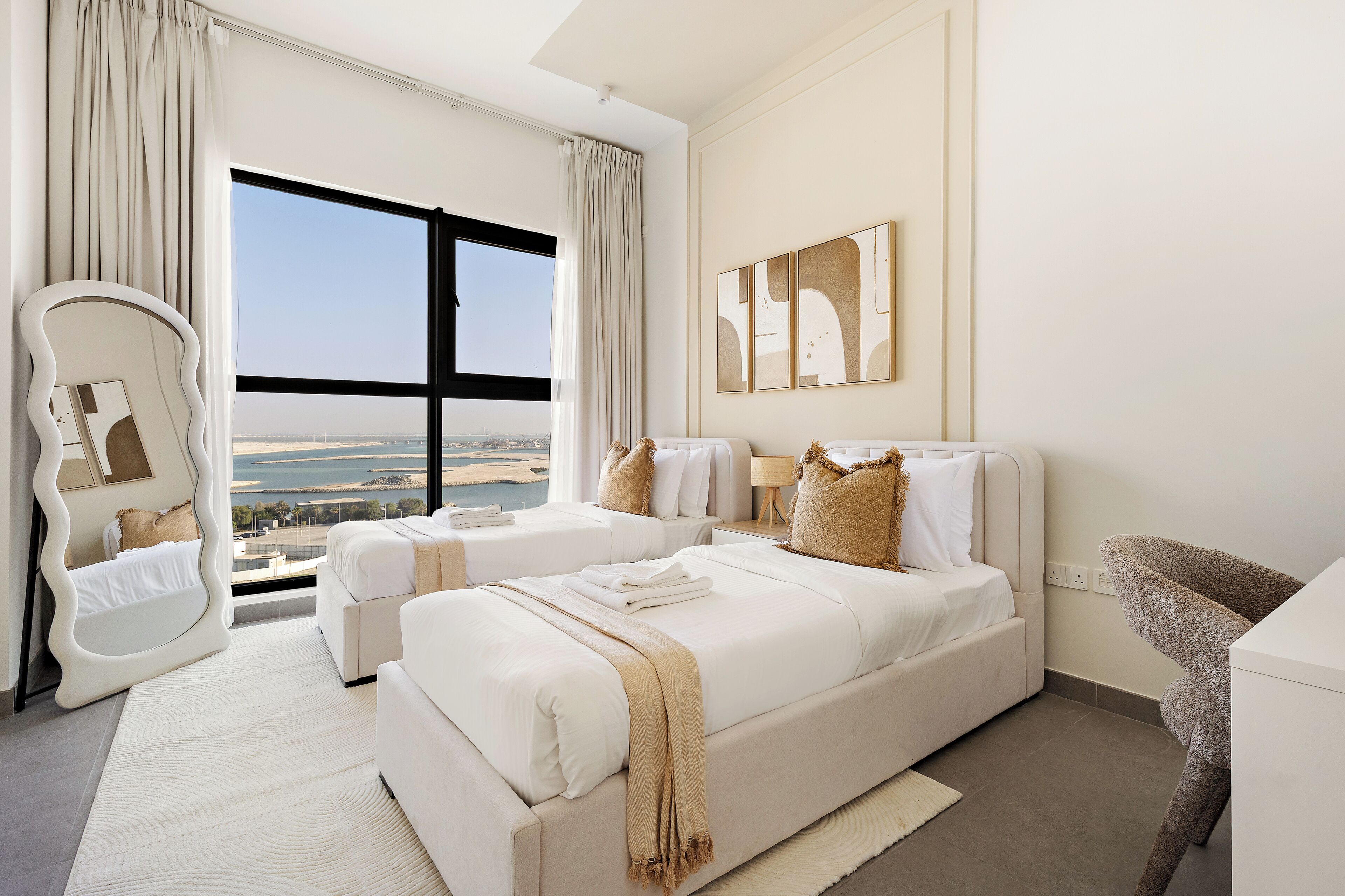 Habitació d'hotel amb dos llits, una finestra gran amb vista a la ciutat, un mirall i una obra d'art abstracta a la paret.