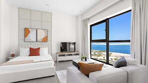 Ein modernes Hotelzimmer mit Bett, Sofa, Fernseher und einem großen Fenster mit Meerblick.