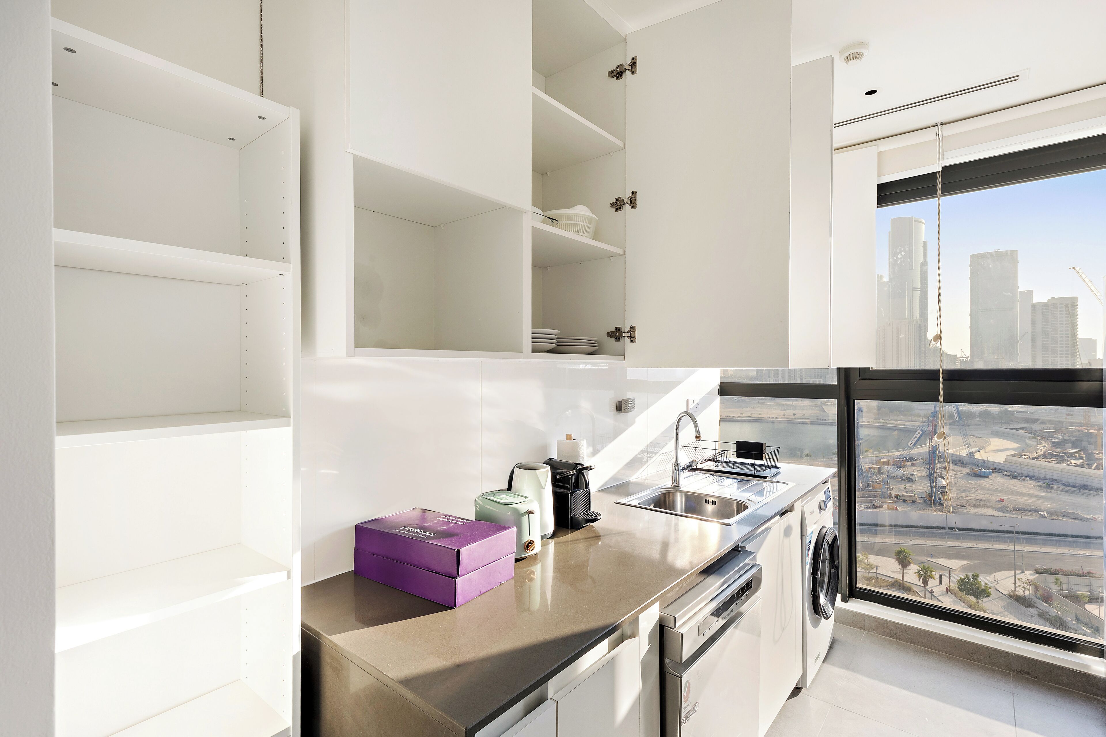 Une cuisine moderne dotée d’un lave-linge intégré, d’une grande fenêtre offrant une vue sur la ville et d’un design minimaliste.
