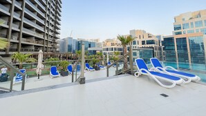 A rooftop pool area with blue lounge chairs, a palm tree, and modern buildings in the background. - Unforgettable 1BR Burj Khalifa Views (Dubai)