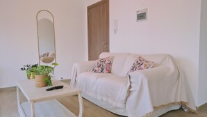 Ein gemütliches Wohnzimmer mit einer Couch, einem kleinen Tisch, einer Topfpflanze und einem Wandspiegel.