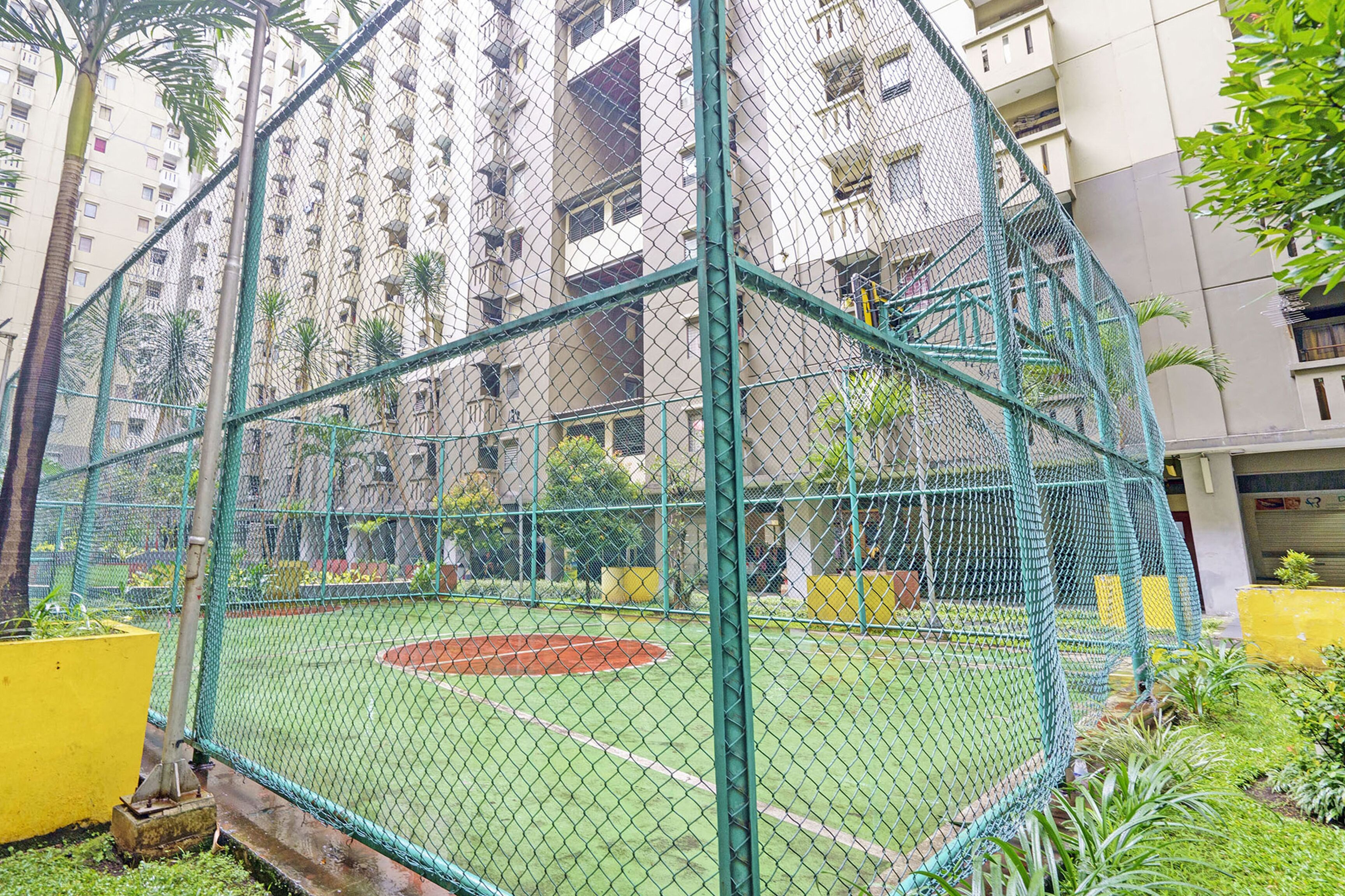 A fenced sports court with a green field, surrounded by a tall residential building.