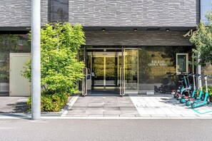 A modern building entrance with a glass door, a small tree, and electric scooters parked outside. - ESLEAD HOTEL Osaka Ebisu (Osaka)