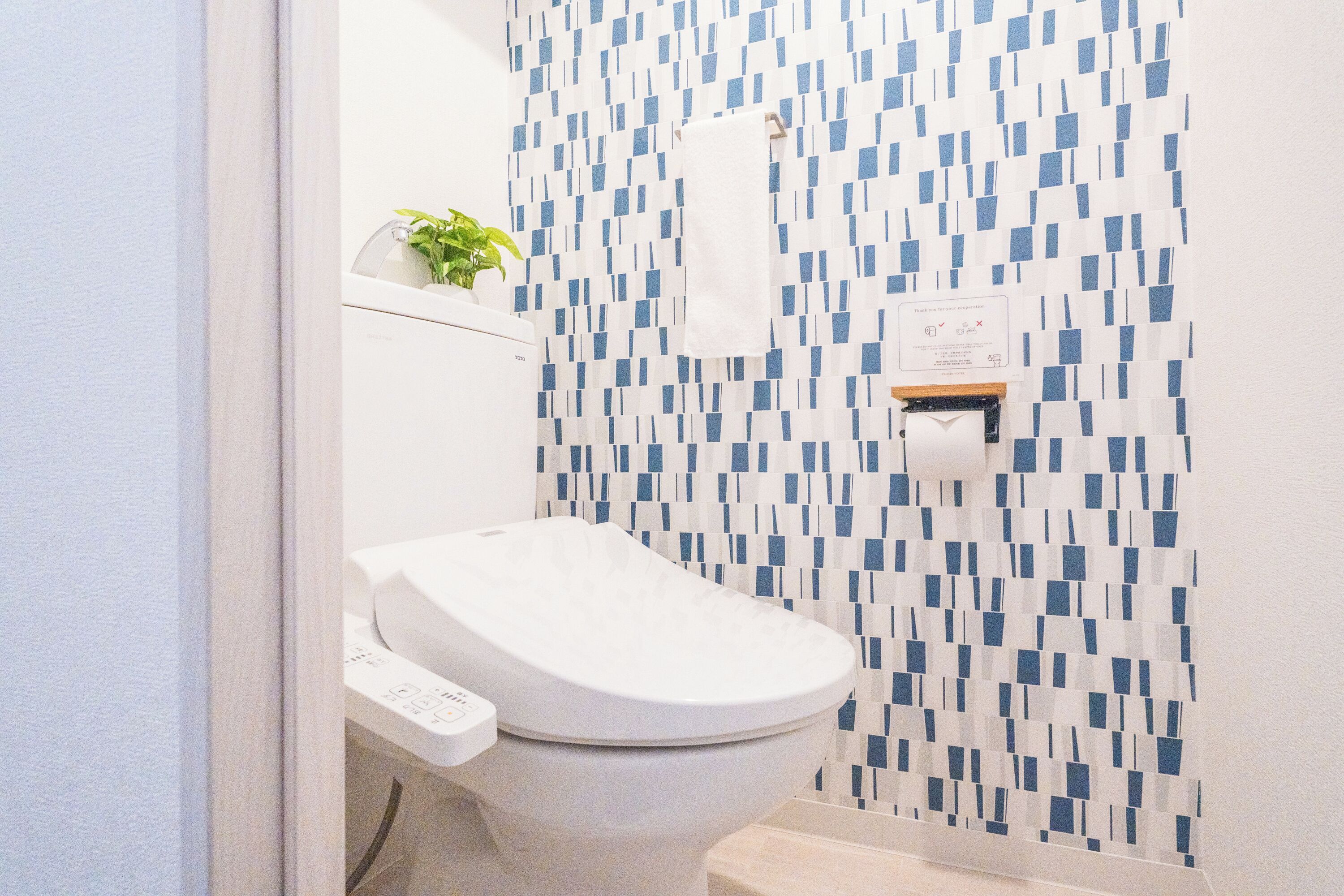 Un bagno con un water bianco, un dispenser di asciugamani di carta a parete e una piccola pianta in vaso.