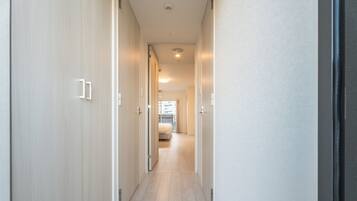 A narrow hallway with wooden flooring leading to a bedroom with a bed and a window.