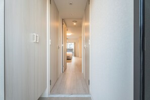 A narrow hallway with wooden flooring leading to a bedroom with a bed and a window. - ESLEAD HOTEL Osaka Ebisu (Osaka)