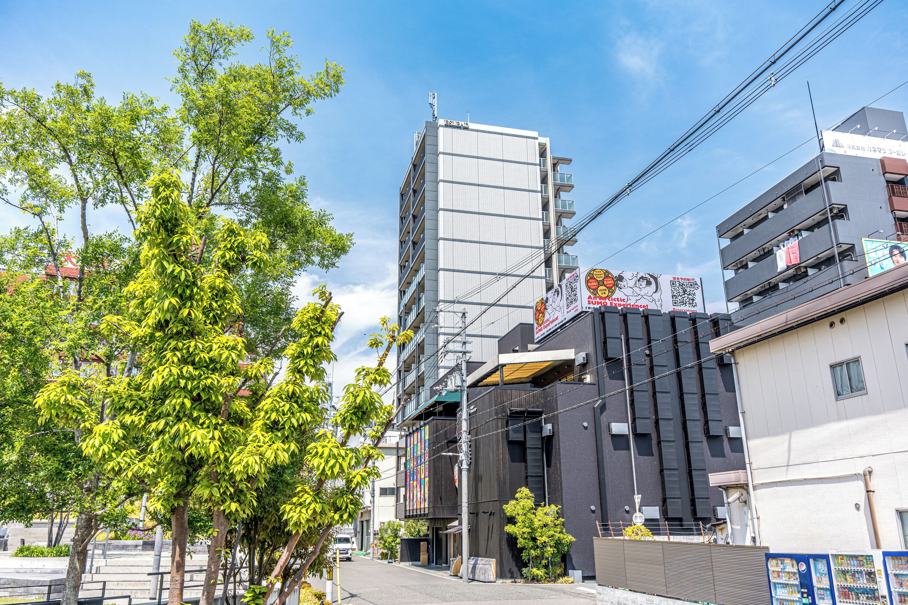 Un bâtiment moderne à plusieurs étages, doté d’un parking et situé dans une rue bordée d’arbres.