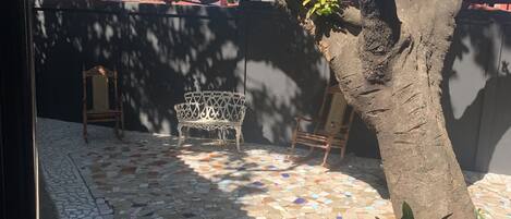 A courtyard with a tiled floor, a large tree, and a metal bench.