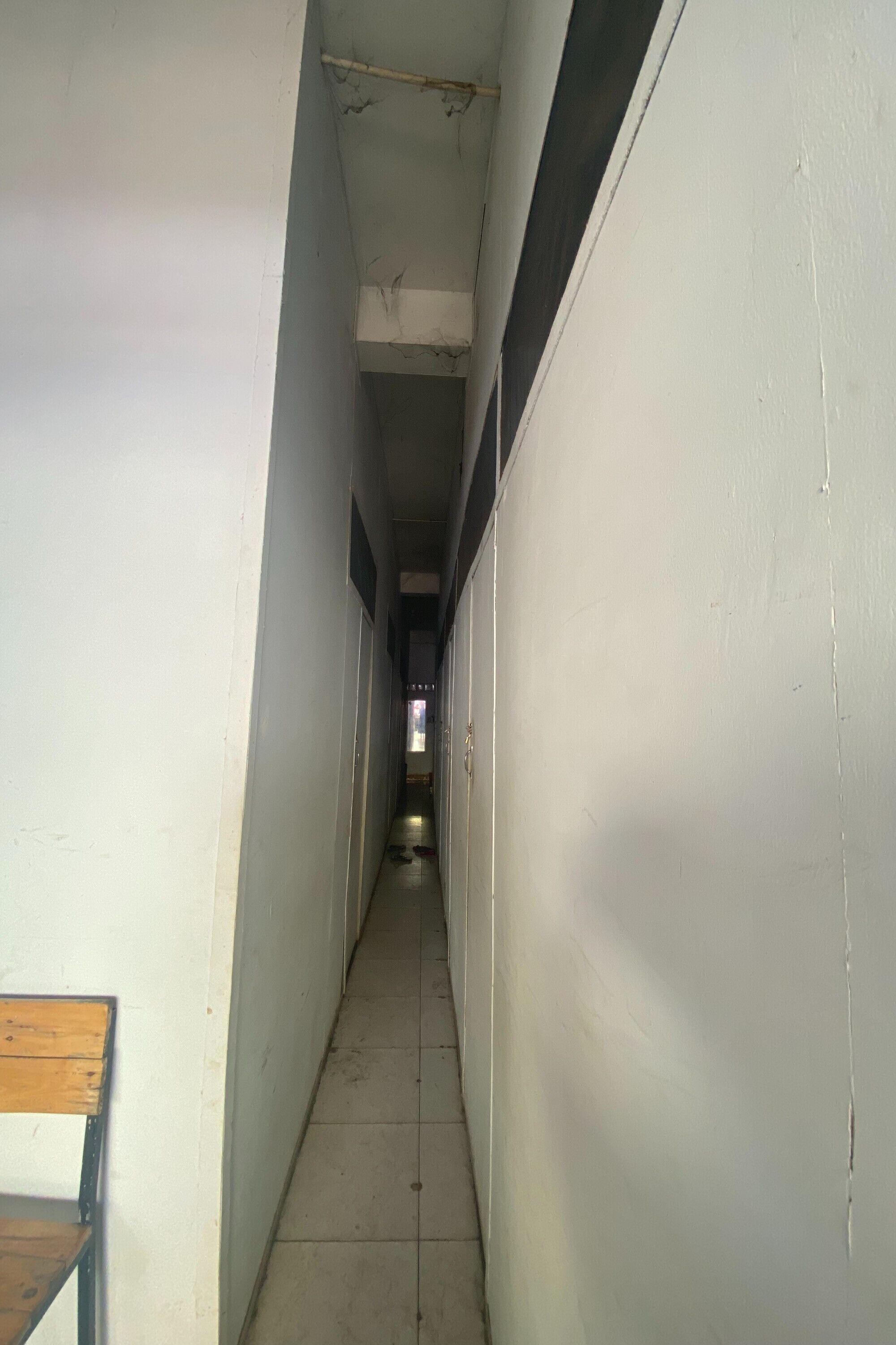 Un pasillo estrecho con paredes blancas y un banco de madera a la izquierda.